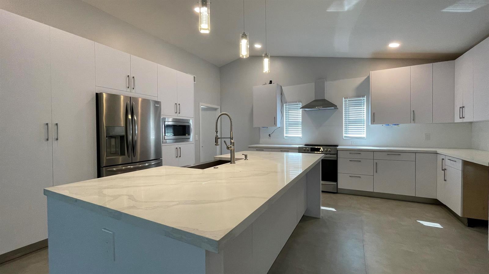A modern kitchen features white cabinetry, a large marble-topped island, and stainless steel appliances — 17548 32nd Lane N, FL 33470, FL