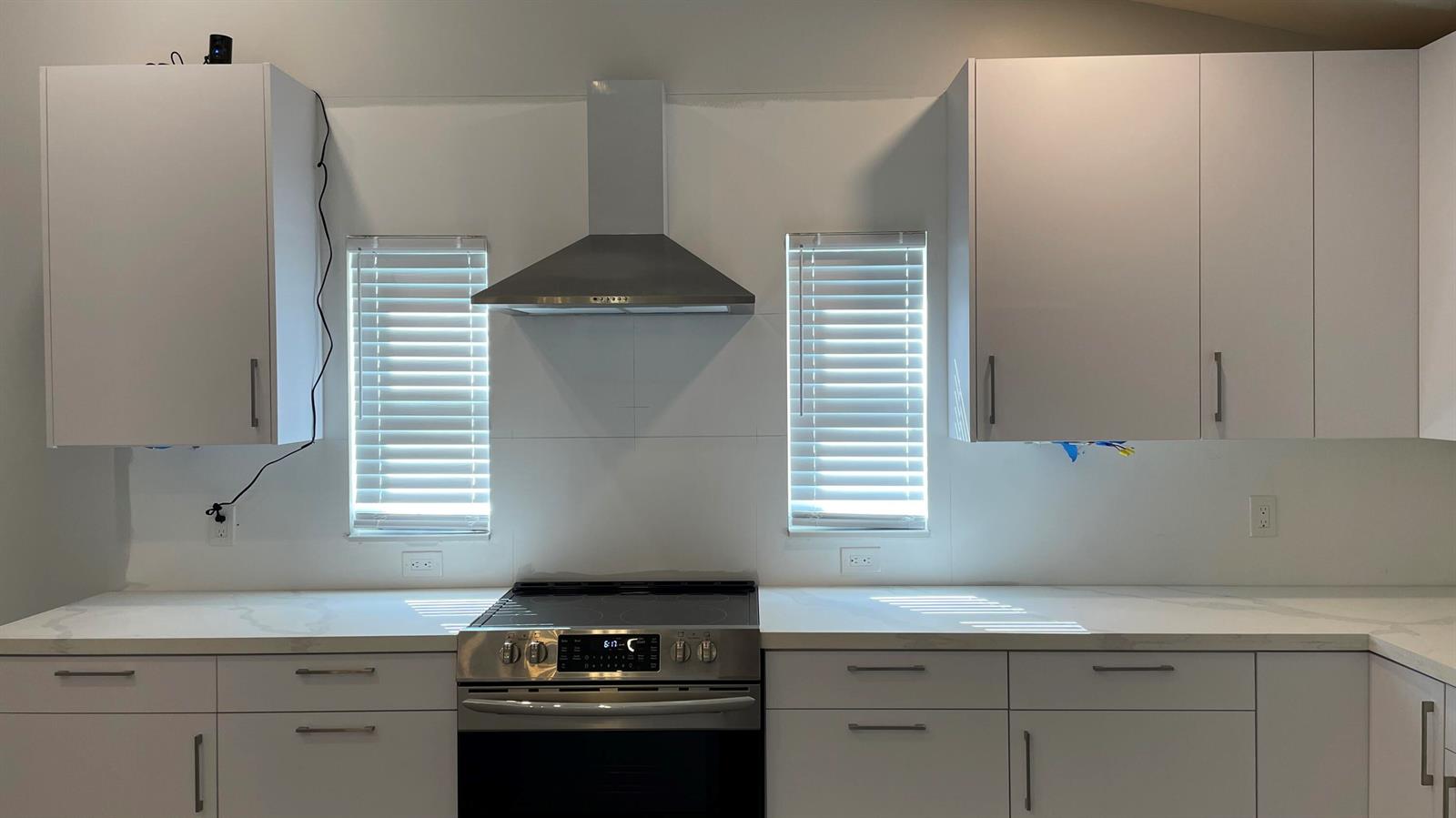 A modern kitchen features white cabinets, stainless steel appliances, a range hood, and quartz countertops — 17548 32nd Lane N, FL 33470, FL
