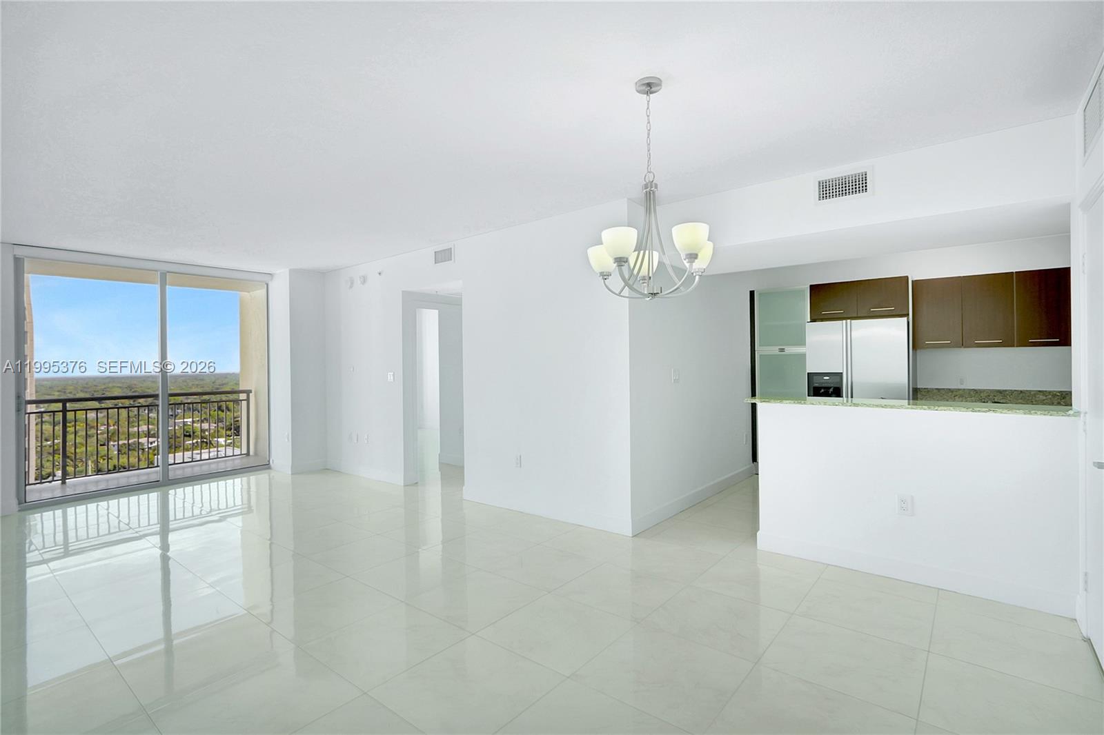 An open-concept living and dining area features white tile floors, a chandelier, and a balcony — 9066 SW 73rd Ct # 1701, Miami FL 33156, MIAMI, FL