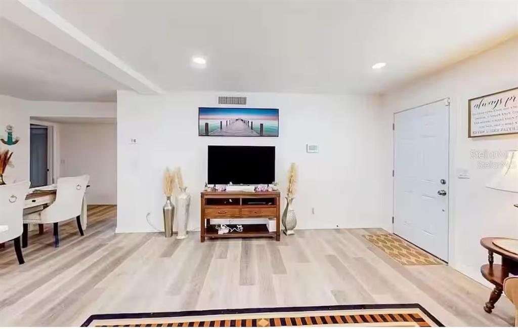 A living room features light wood-look flooring, a television on a wooden console, and a white door — 2760 KUMQUAT DRIVE UNIT 001, CLEARWATER, FL