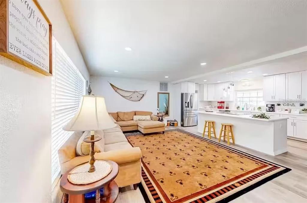 An open-concept living room and kitchen featuring a tan sectional, area rug, and white cabinetry — 2760 KUMQUAT DRIVE UNIT 001, CLEARWATER, FL
