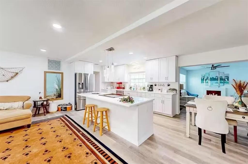 A bright, open-concept kitchen features white cabinetry, a central island with stools, and wood flooring — 2760 KUMQUAT DRIVE UNIT 001, CLEARWATER, FL