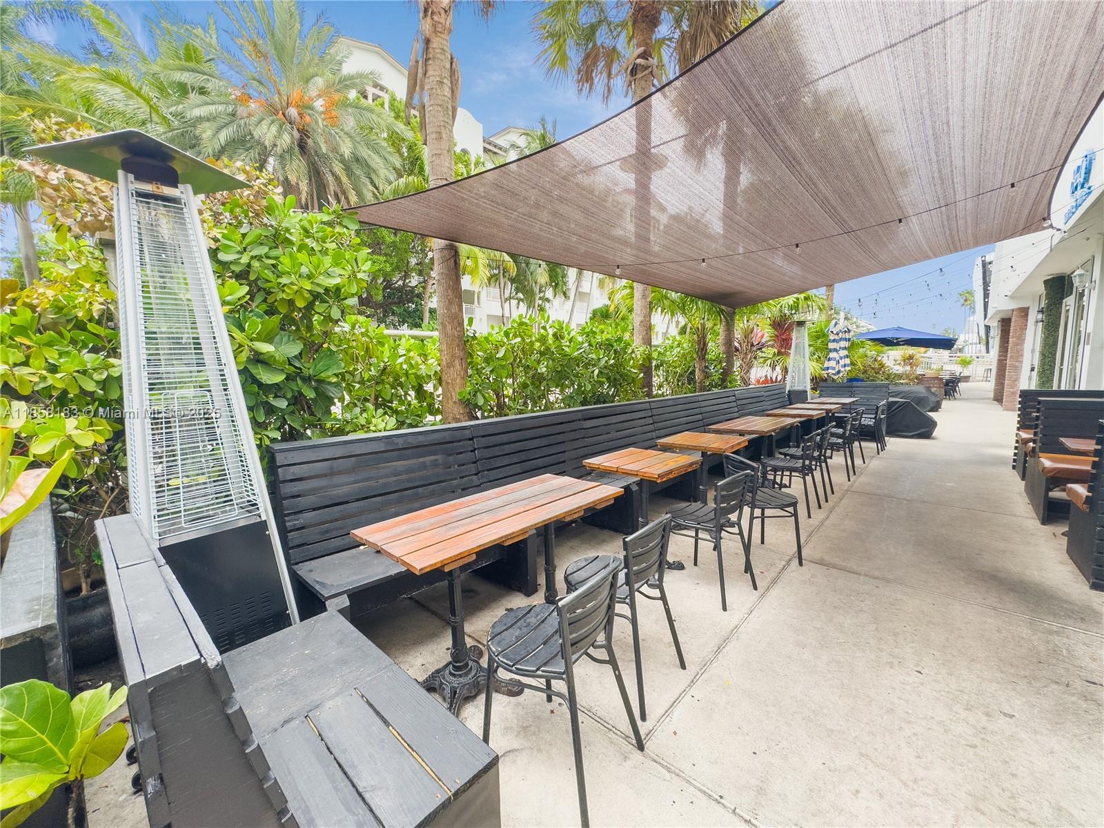 An outdoor patio features wooden tables, black chairs, a long bench, and a shade sail — 1410 20th St # 1418, Miami Beach FL 33139, MIAMI BEACH, FL