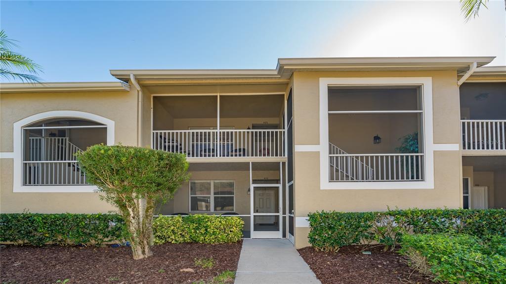 A two-story apartment building exterior features screened-in balconies, beige stucco walls, and a landscaped walkway — 5241 MAHOGANY RUN AVENUE UNIT 425, SARASOTA, FL