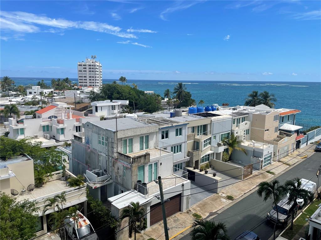An elevated view shows coastal residential buildings, palm trees, a street, and the ocean — 1 INGA STREET UNIT 6H, SAN JUAN, PR