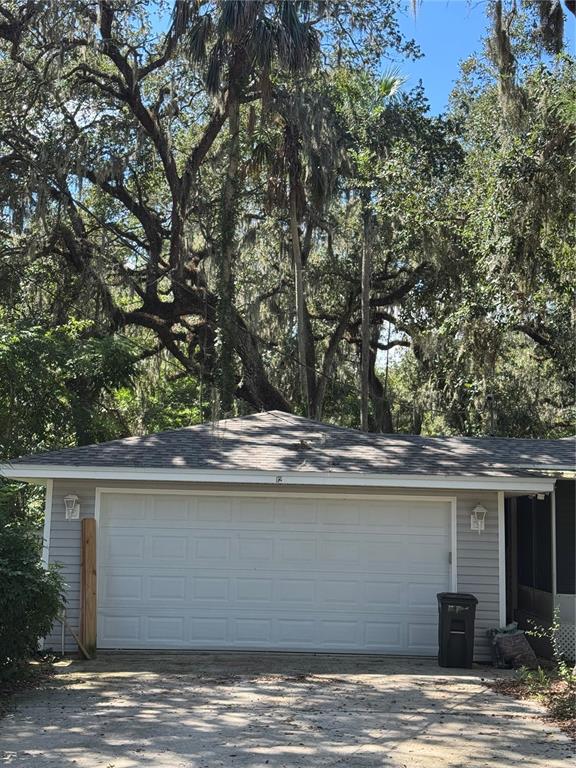 A detached garage with a white door and gray siding sits under large oak trees — 12 DAWSON DRIVE, PALM COAST, FL