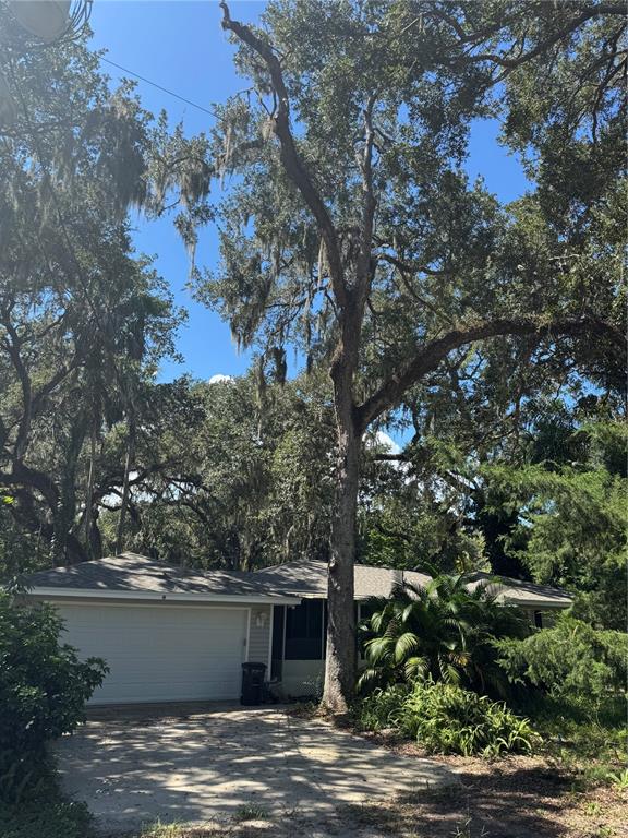 A single-story house with a white garage door is surrounded by large, moss-draped oak trees — 12 DAWSON DRIVE, PALM COAST, FL