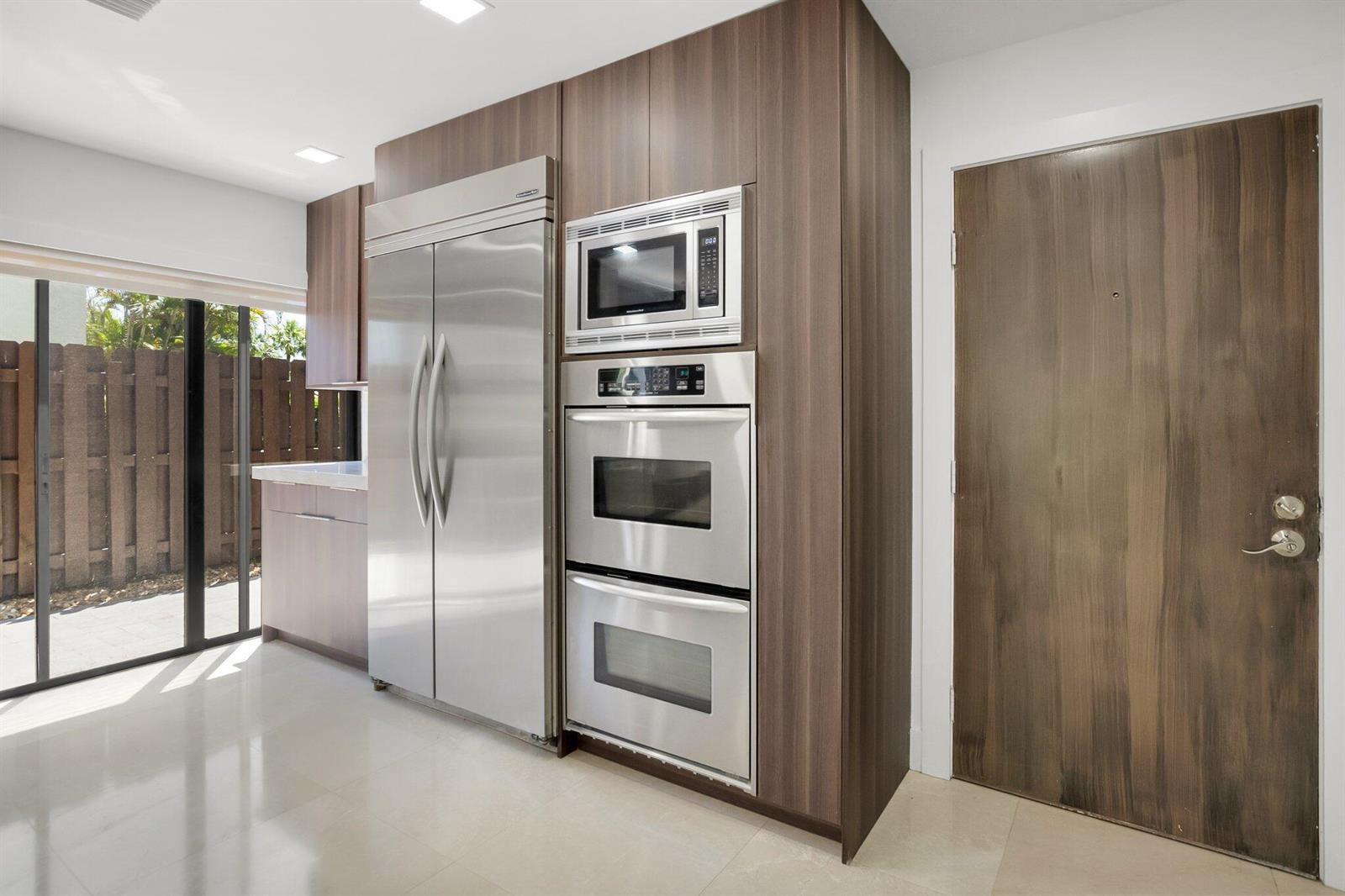 A modern kitchen features stainless steel appliances, wood-grain cabinetry, and a sliding glass door — 21922 Cypress Drive # 37b, Boca Raton FL 33433, BOCA RATON, FL