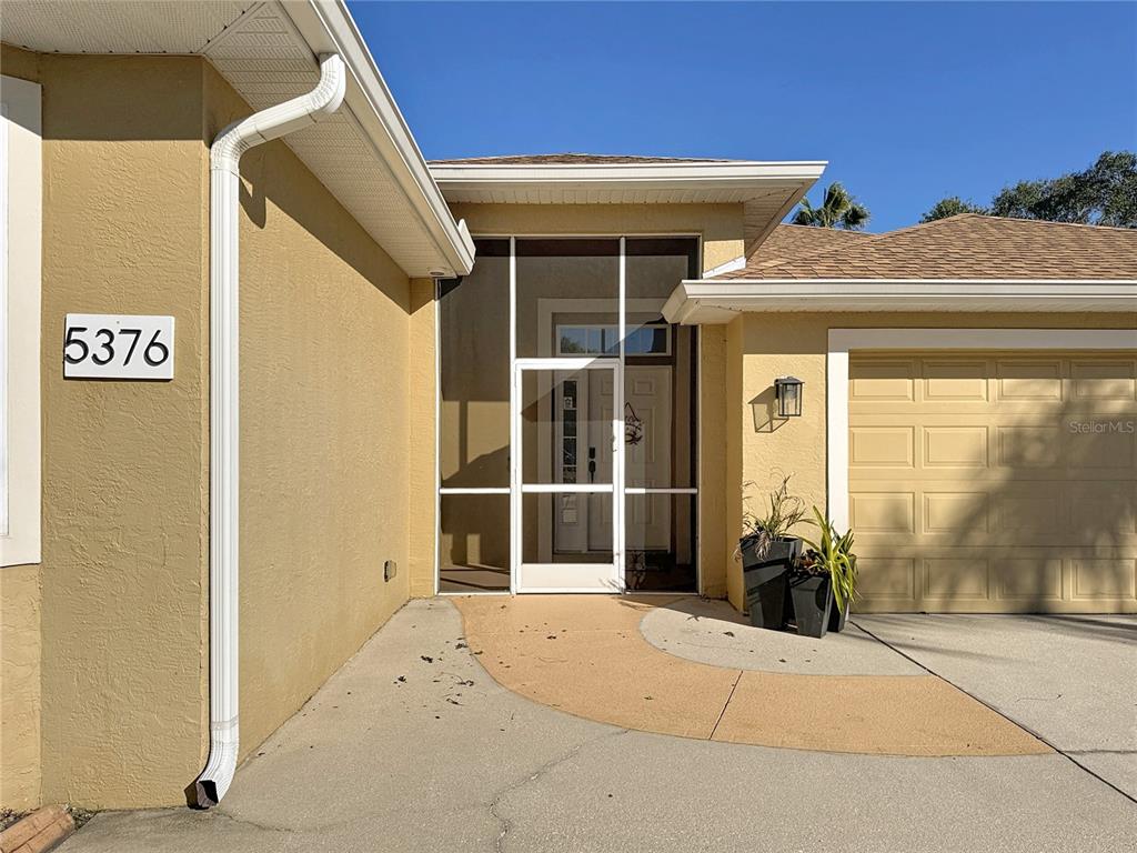 The exterior of a house features a tan stucco facade, a screen door, and a garage — 5376 LEVI LANE, SARASOTA, FL
