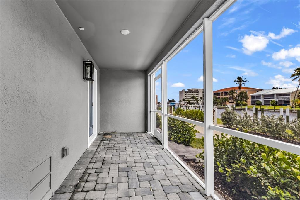 A screened-in patio with gray paver flooring overlooks a canal and neighboring buildings — 1617 SEAHAVEN DRIVE UNIT 505, PUNTA GORDA, FL