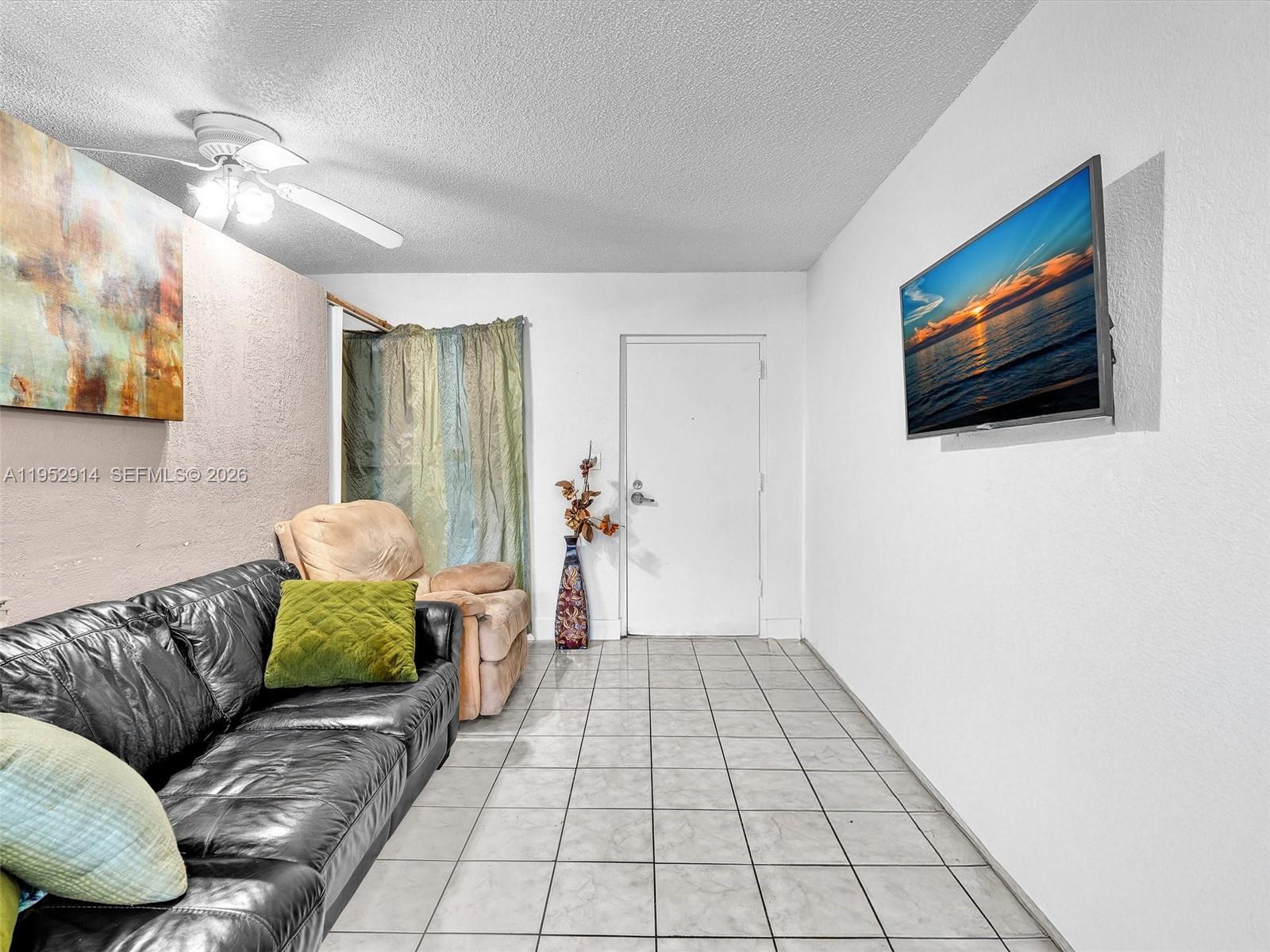A living room features a black leather sofa, a beige recliner, and a wall-mounted television — 13500 NE 3rd Ct # 121, North Miami FL 33161, NORTH MIAMI, FL