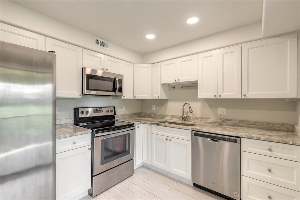 A kitchen with white cabinets, stainless steel appliances, and stone countertops — 275 INDIGO DRIVE UNIT 204, DAYTONA BEACH, FL