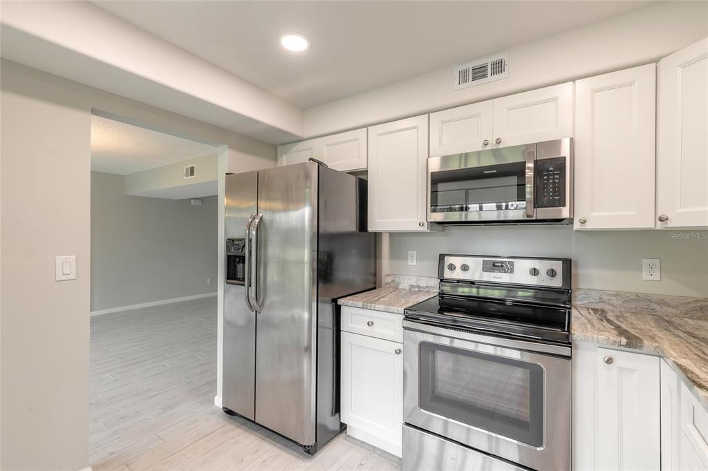 A kitchen features white cabinets, stainless steel appliances, and a marble-patterned countertop — 275 INDIGO DRIVE UNIT 204, DAYTONA BEACH, FL