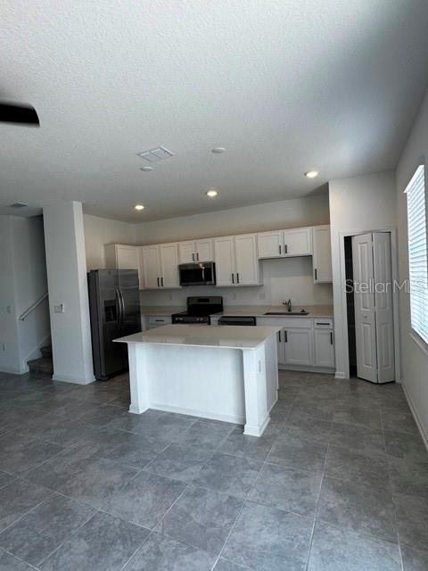 A kitchen features white cabinets, a central island, stainless steel appliances, and gray tile flooring — 2500 SKYLINE LOOP, KISSIMMEE, FL