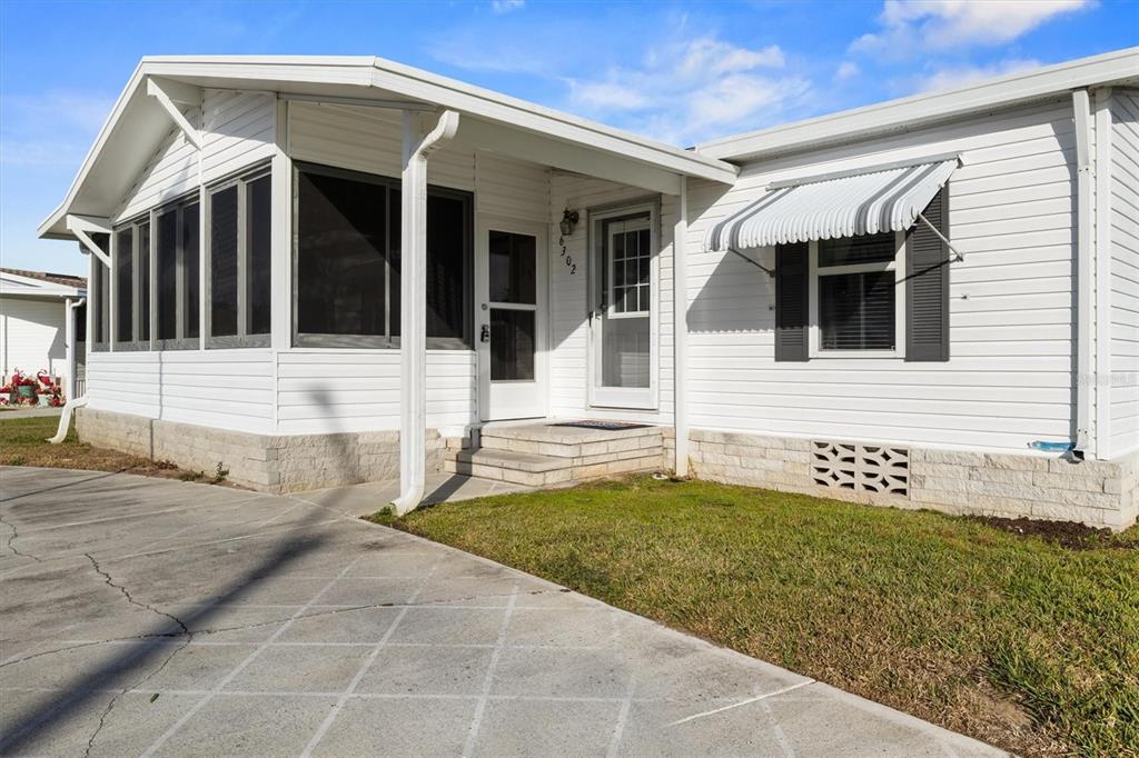 A white mobile home exterior features a screened-in porch, a concrete driveway, and a small lawn — 6302 TREASURE VALLEY LOOP, LAKE WALES, FL