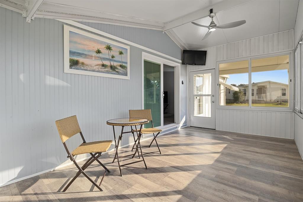 A sunroom features light wood-look flooring, a ceiling fan, a small bistro set, and windows — 6302 TREASURE VALLEY LOOP, LAKE WALES, FL