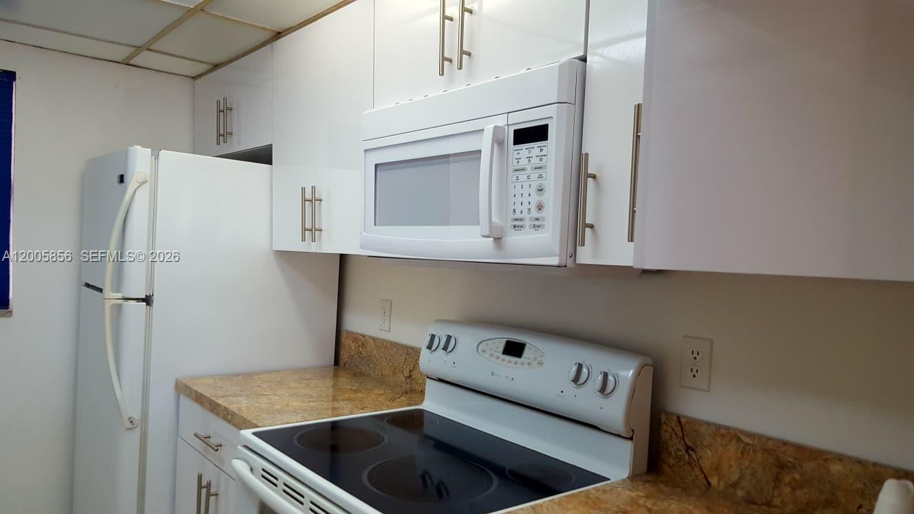A kitchen features white cabinets, a white microwave, a white refrigerator, and a stove — 19701 SW 114th Ave # 266, Miami FL 33157, MIAMI, FL