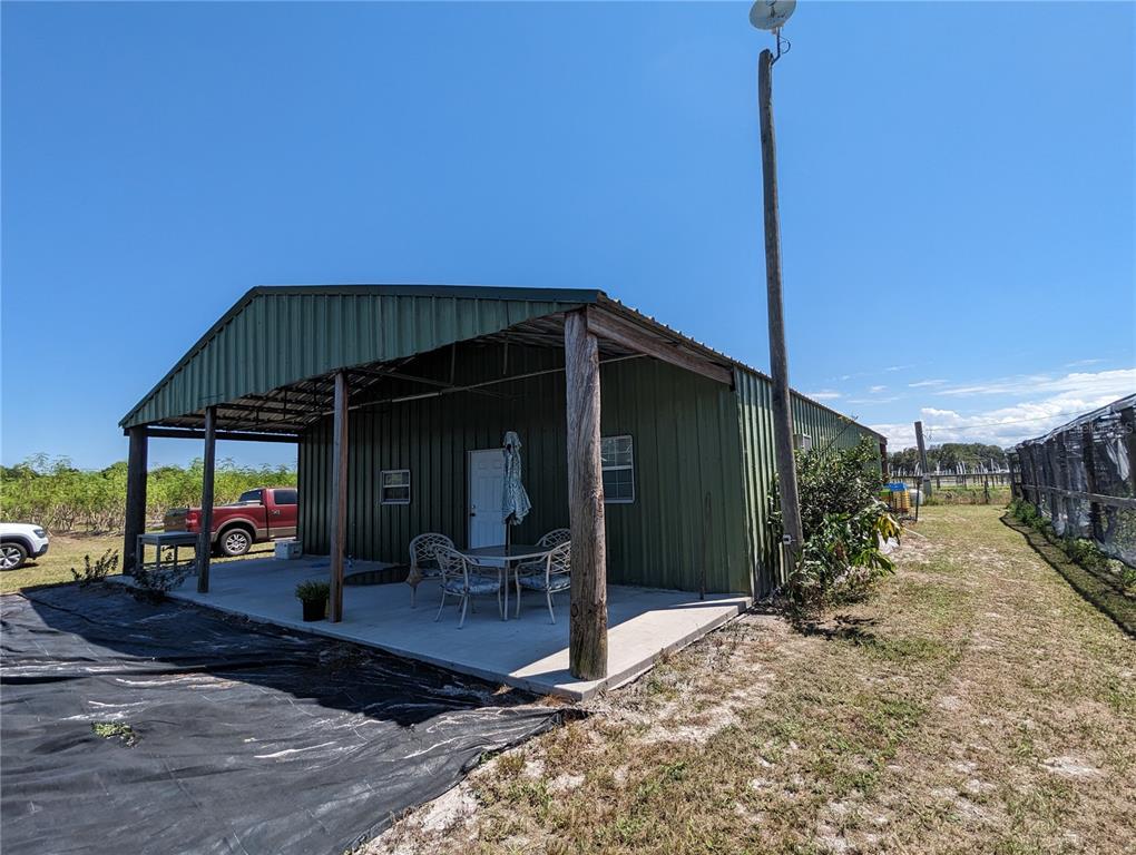 A green metal building features a covered concrete patio with outdoor furniture and wooden posts — 16070 CARLTON LAKE ROAD, WIMAUMA, FL