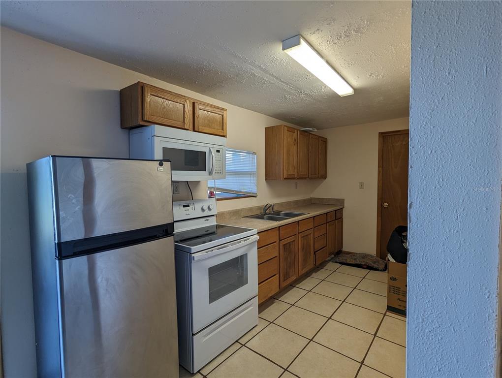 A kitchen features stainless steel appliances, wood cabinets, laminate countertops, and light-colored tile flooring — 16070 CARLTON LAKE ROAD, WIMAUMA, FL