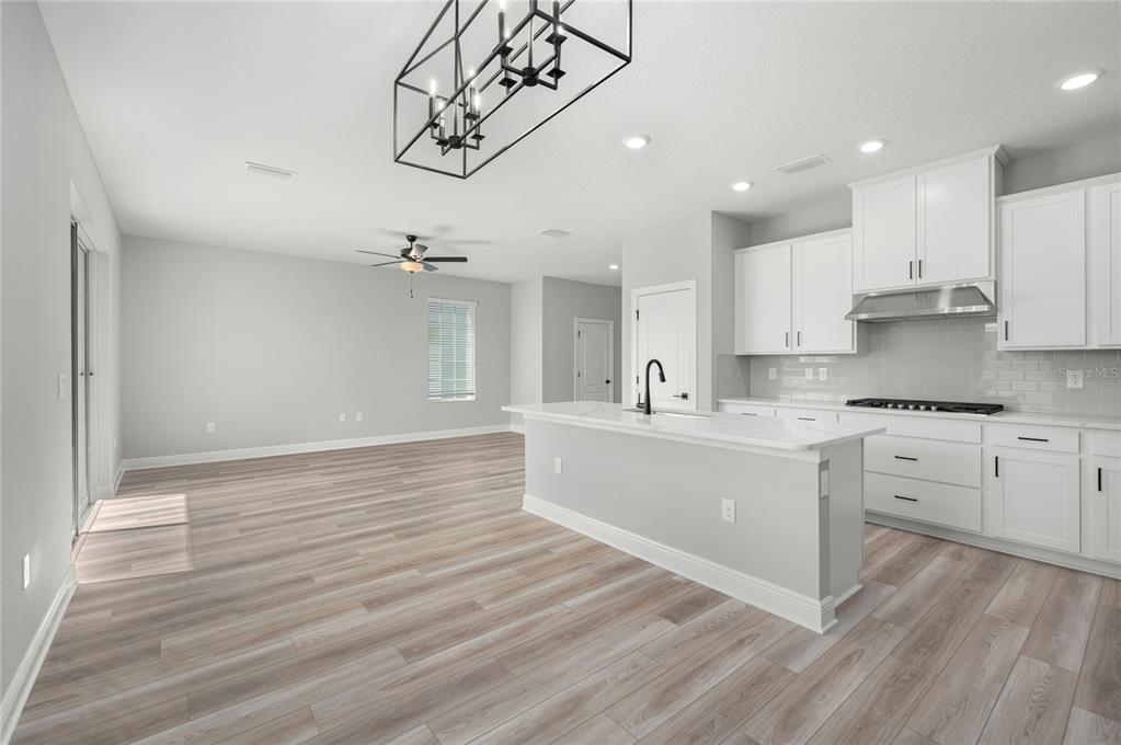 A kitchen with white cabinets and a center island opens into a living area — 7886 SOMERSWORTH DRIVE, KISSIMMEE, FL