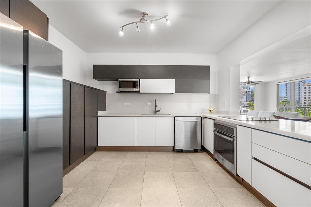 A modern kitchen features white lower cabinets, dark upper cabinets, stainless steel appliances, and tile flooring — 59 LIRIO UNIT 301, CAROLINA, PR