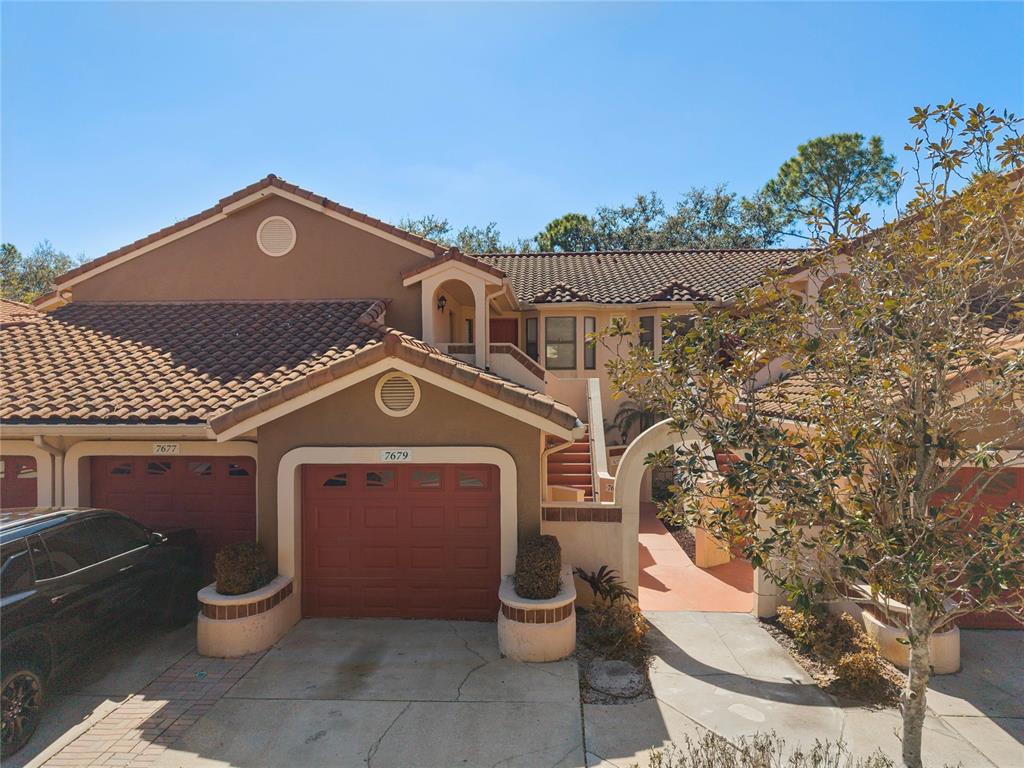 A two-story townhouse exterior features a brown stucco facade, tile roof, and attached garages — 7679 SUGAR BEND DRIVE UNIT 7784, ORLANDO, FL