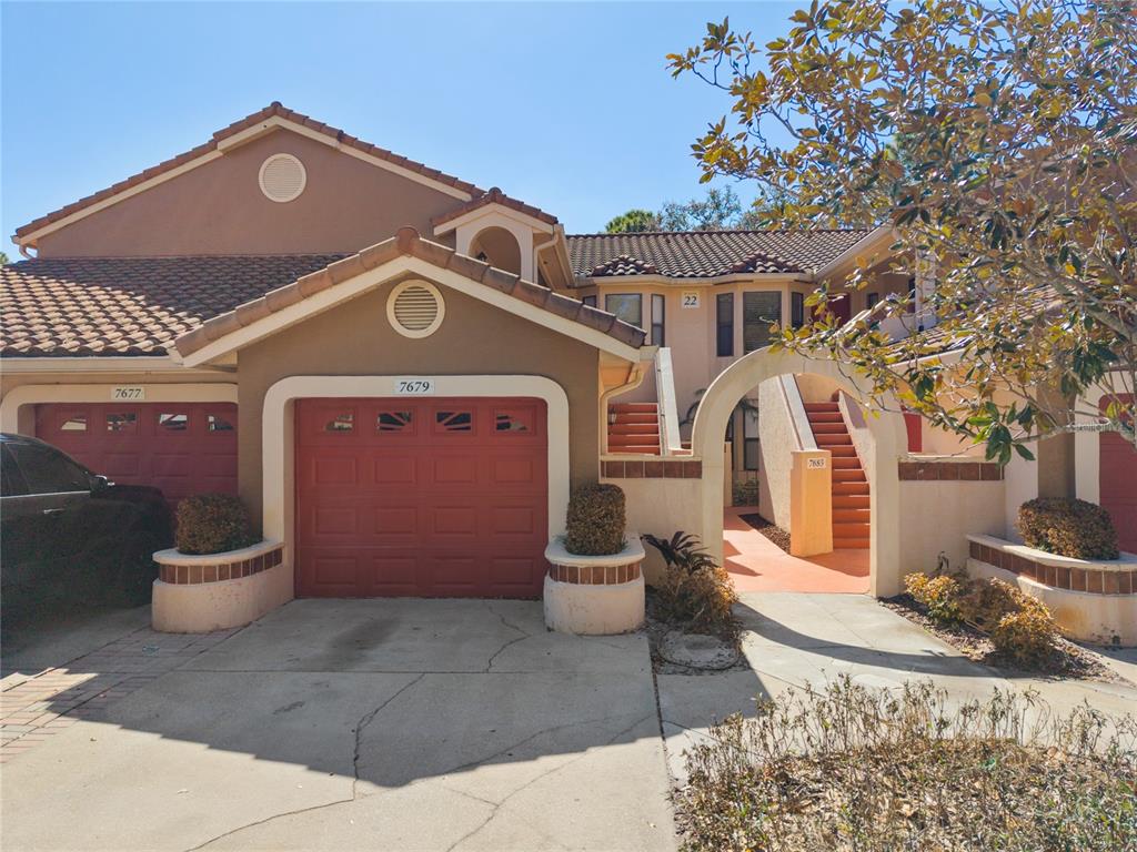 A two-story residential building features a red garage door, a tiled roof, and exterior stairs — 7679 SUGAR BEND DRIVE UNIT 7784, ORLANDO, FL