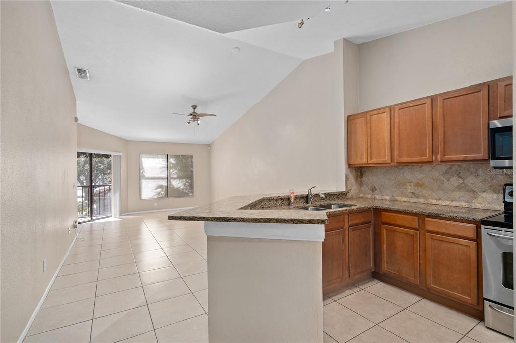 A kitchen with wood cabinets and granite countertops overlooks an open-concept living area with tile — 7679 SUGAR BEND DRIVE UNIT 7784, ORLANDO, FL