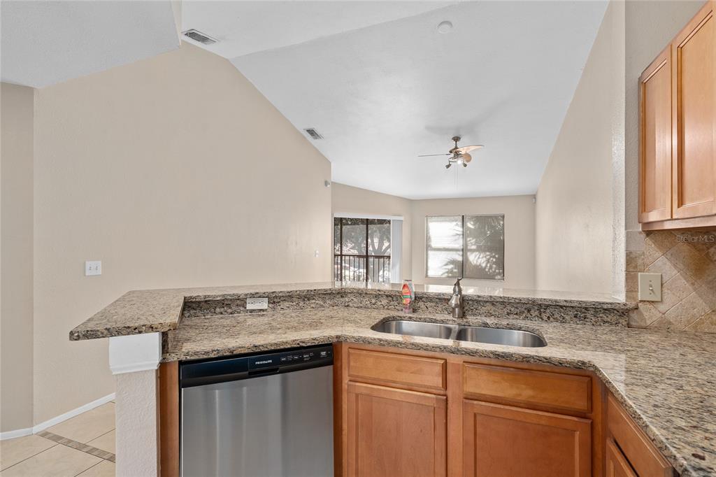A kitchen with granite countertops, a stainless steel dishwasher, and a view into the living area — 7679 SUGAR BEND DRIVE UNIT 7784, ORLANDO, FL