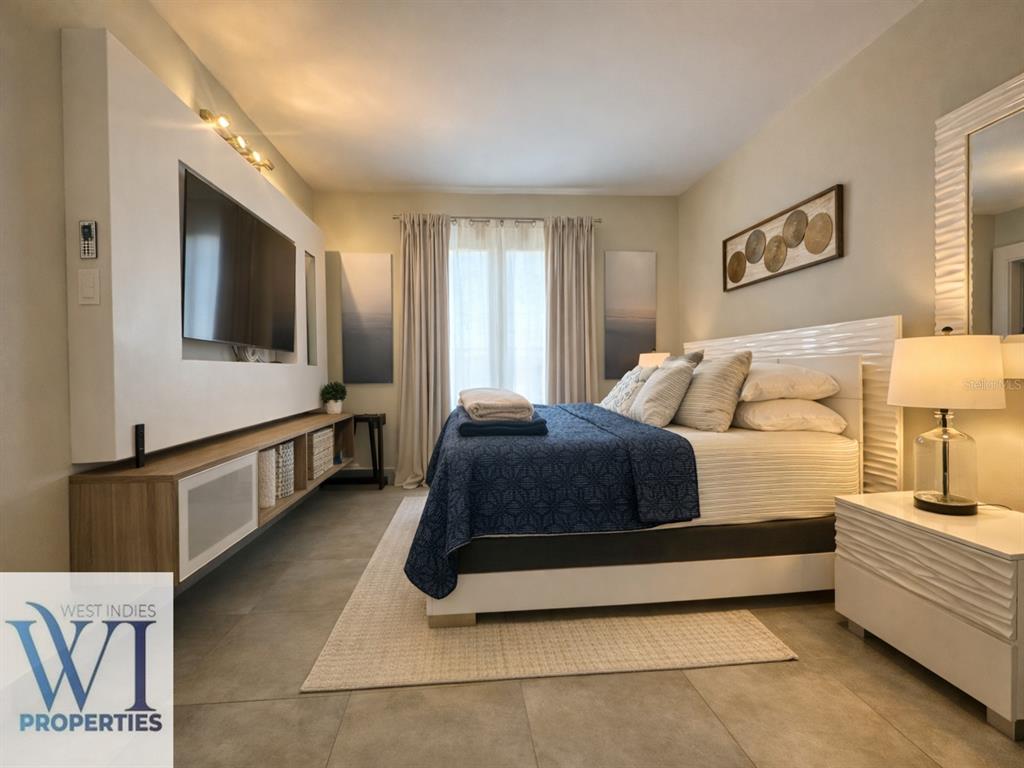 A modern bedroom features a large wall-mounted television, a blue quilt, and light-colored furniture — 201 DORADO DEL MAR BLVD UNIT 2656, DORADO, PR