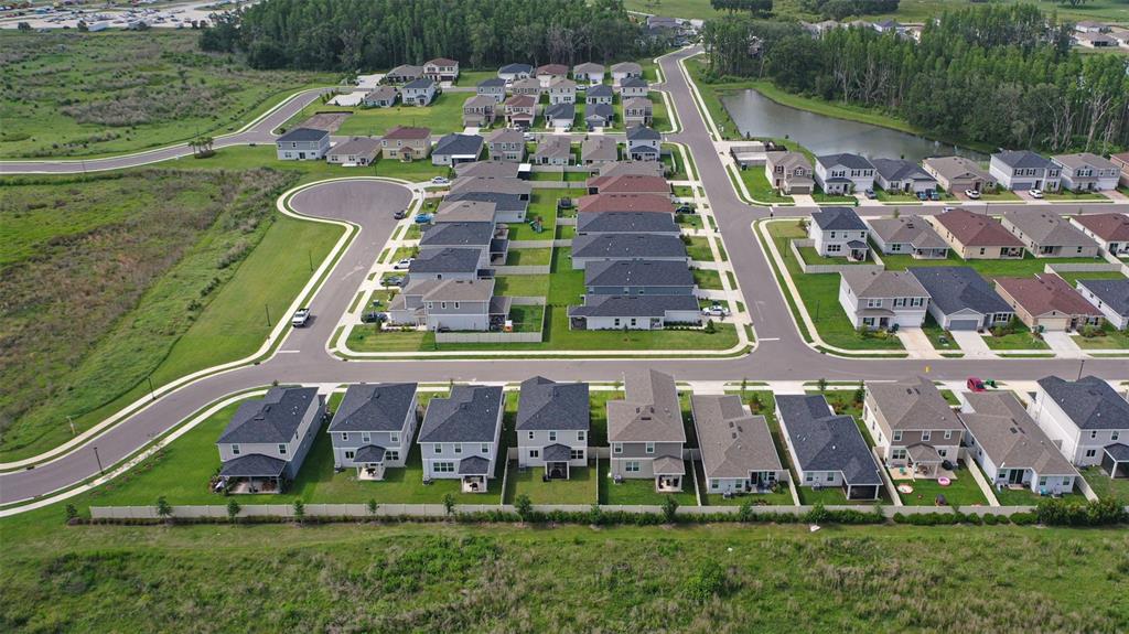 An aerial view shows a suburban neighborhood with rows of houses, paved streets, and a pond — 37402 YUKON DRIVE, ZEPHYRHILLS, FL