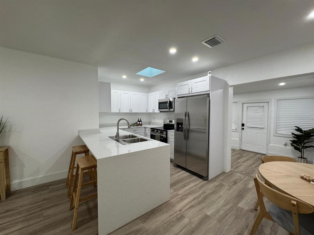 A kitchen features white cabinetry, quartz countertops, stainless steel appliances, and wood-look flooring — 22011 CATHERINE AVENUE, PORT CHARLOTTE, FL