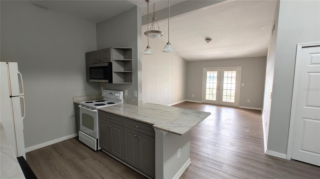 A kitchen with gray cabinets and a breakfast bar opens into a living area — 145 N PEARL LAKE CAUSEWAY UNIT 204, ALTAMONTE SPRINGS, FL