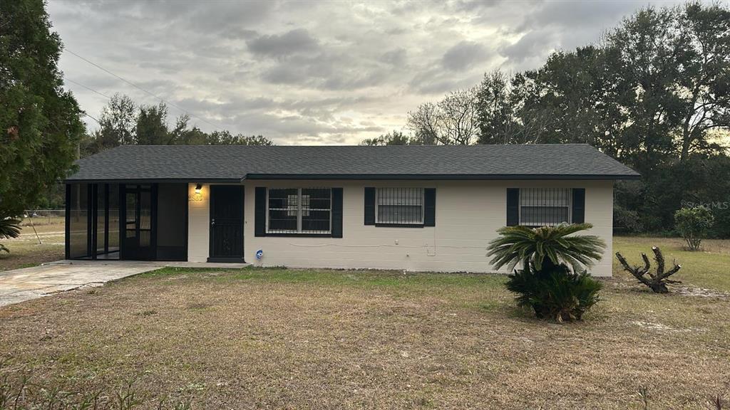 A single-story house with a screened-in porch, beige exterior, and dark roof under a cloudy sky — 2863 COUNTY ROAD 238 UNIT 238, WILDWOOD, FL