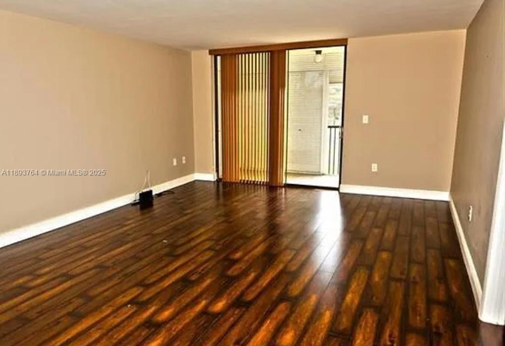 An empty room features dark wood-look flooring, beige walls, and a sliding glass balcony door — 5570 NW 44th St # 312A, Lauderhill FL 33319, LAUDERHILL, FL