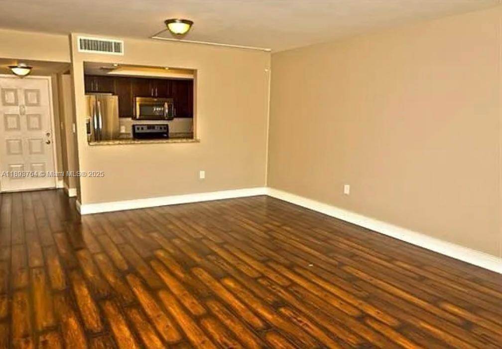 An empty living room features dark wood-look flooring and a pass-through window to the kitchen — 5570 NW 44th St # 312A, Lauderhill FL 33319, LAUDERHILL, FL