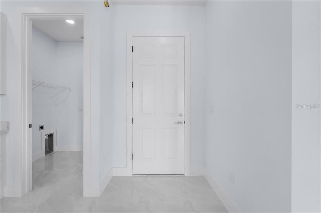 A white door stands between a laundry room and a plain wall on tiled floors — 1927 RICHMOND AVENUE N, LEHIGH ACRES, FL