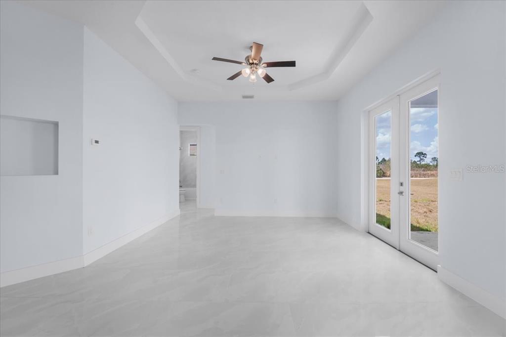 A bright, empty room features white tile floors, a tray ceiling, and glass double doors — 1927 RICHMOND AVENUE N, LEHIGH ACRES, FL