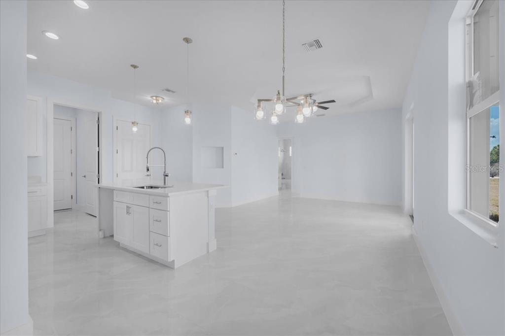 A bright, open-concept kitchen and living area featuring white cabinetry, a center island, and tile flooring — 1927 RICHMOND AVENUE N, LEHIGH ACRES, FL