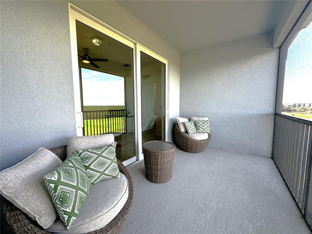 A covered balcony features wicker chairs with patterned pillows, a small table, and sliding glass doors — 14061 HERITAGE LANDING BOULEVARD UNIT 444, PUNTA GORDA, FL