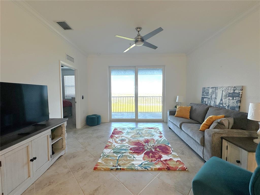 A living room features tile flooring, a floral area rug, a gray sofa, and balcony access — 14061 HERITAGE LANDING BOULEVARD UNIT 444, PUNTA GORDA, FL