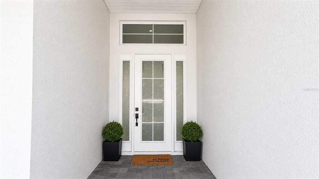 A white front door with glass panels and sidelights sits between two potted topiary trees — 8294 GRANDE SHORES DRIVE, SARASOTA, FL