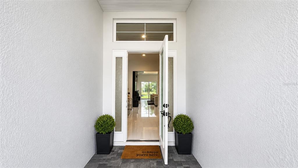 An open front door reveals a bright, tiled entryway with two potted shrubs outside — 8294 GRANDE SHORES DRIVE, SARASOTA, FL