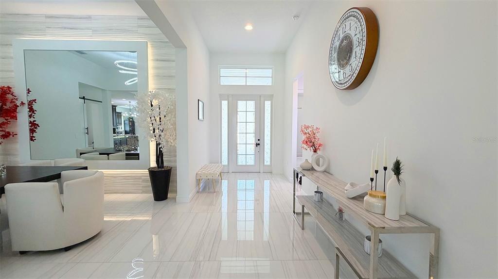 A bright entryway features white tile floors, a console table, and a large wall clock — 8294 GRANDE SHORES DRIVE, SARASOTA, FL