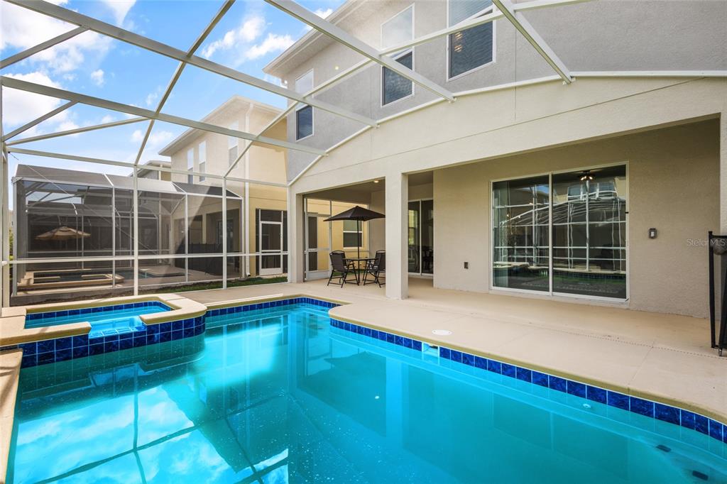 A swimming pool and spa are enclosed within a screened lanai behind a two-story house — 8931 TAKEAWAY WAY, DAVENPORT, FL