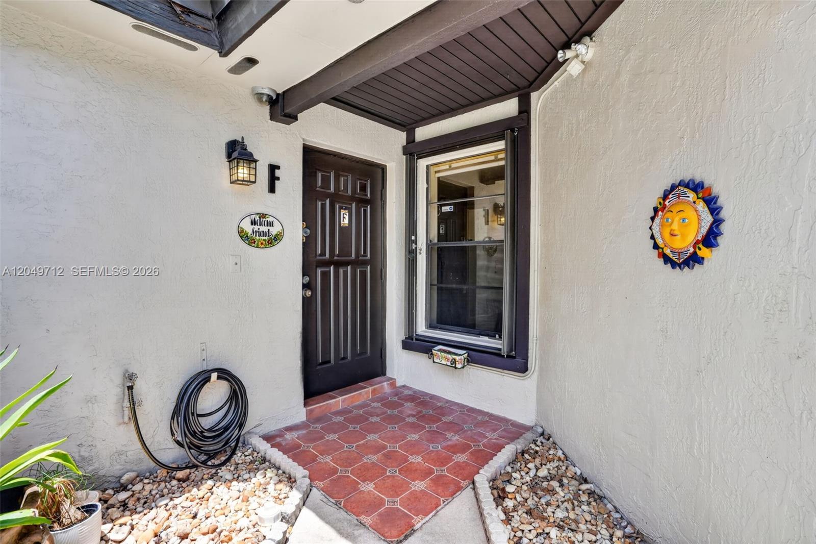 An exterior entryway features a dark door, a window, tiled flooring, and decorative wall art — 15065 SW 49th Ln # F, Miami FL 33185, MIAMI, FL