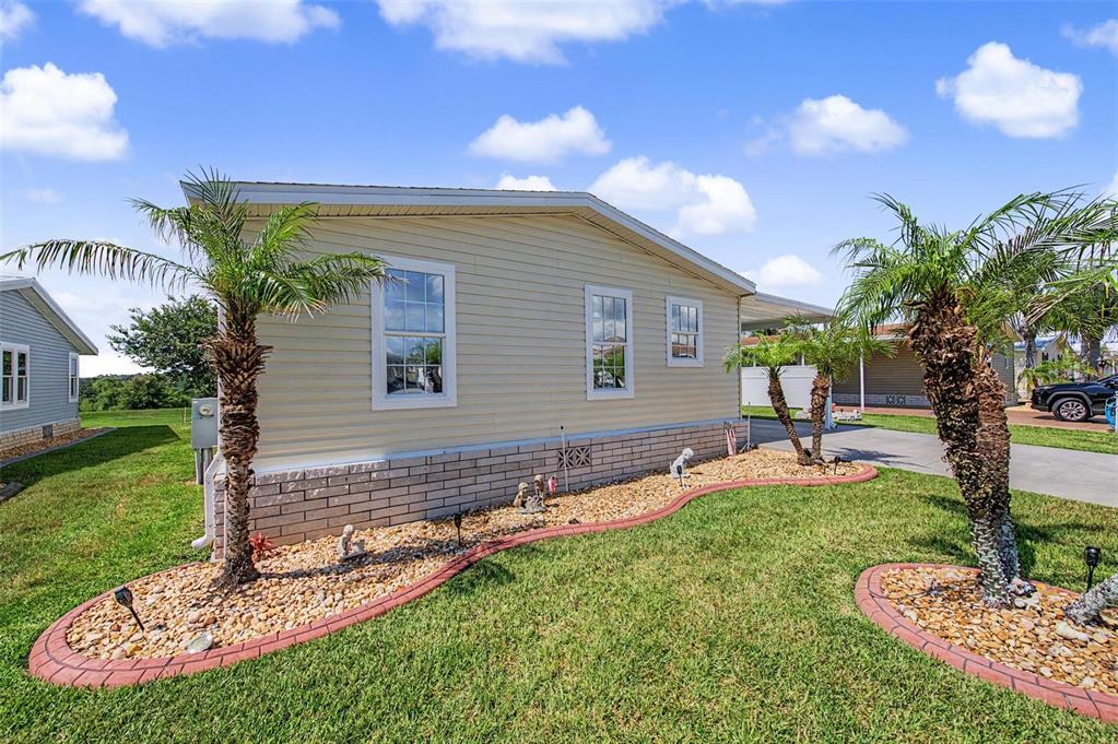 A light-colored manufactured home features a brick base, palm trees, and a landscaped rock bed — 37200 NEUKOM AVENUE, ZEPHYRHILLS, FL