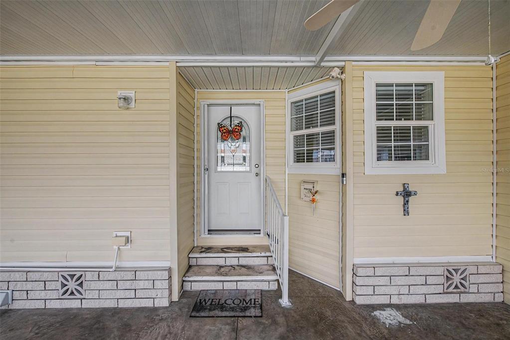 A yellow-sided house exterior features a white front door, two windows, and brick skirting — 37200 NEUKOM AVENUE, ZEPHYRHILLS, FL