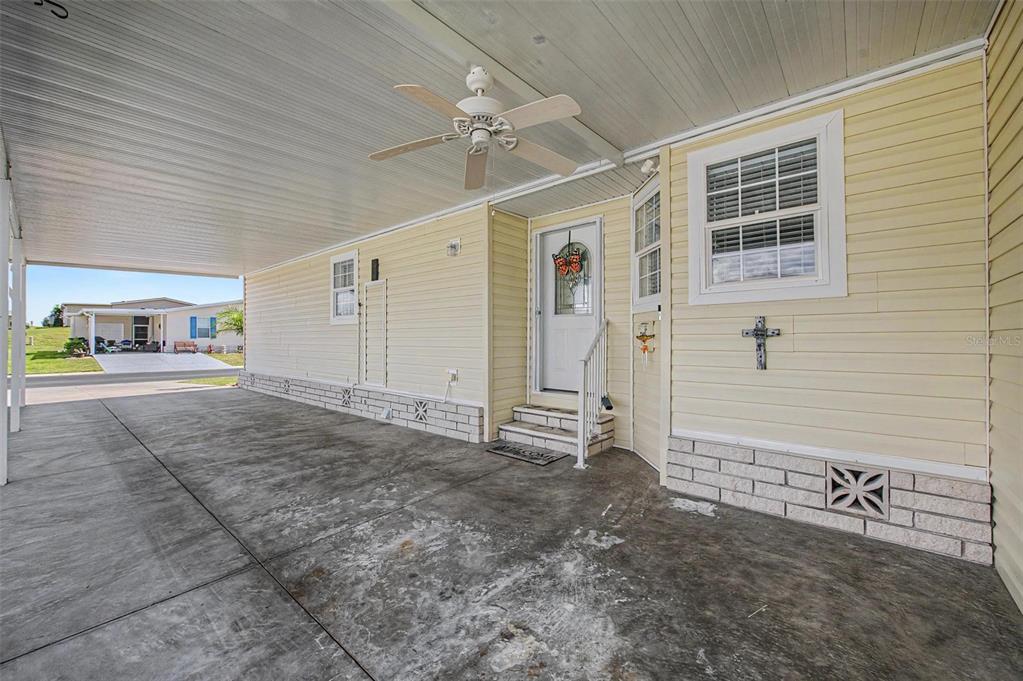 A concrete carport leads to the front entrance of a yellow mobile home — 37200 NEUKOM AVENUE, ZEPHYRHILLS, FL