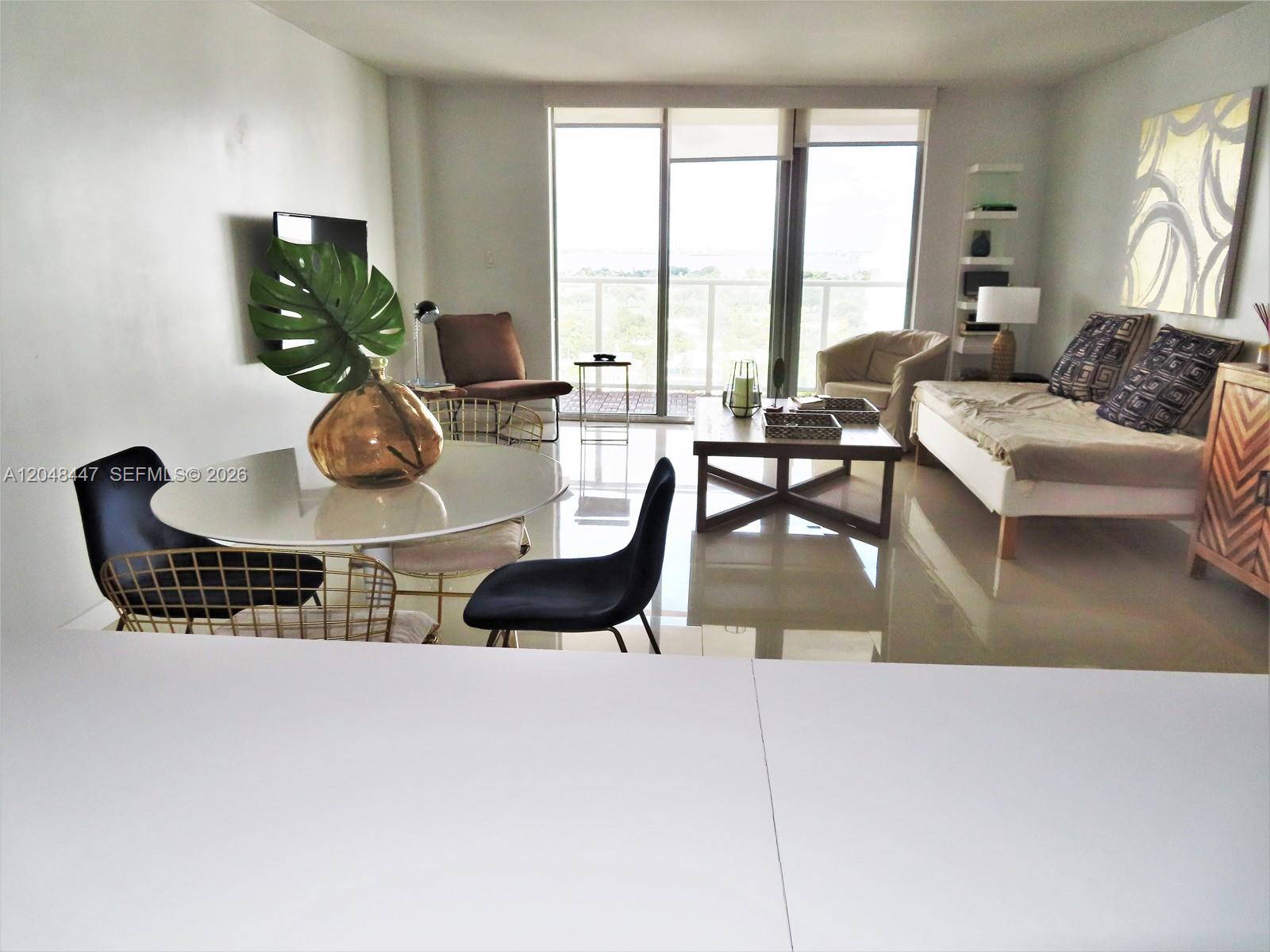 A bright living and dining area features a white table, modern chairs, and balcony access — 5701 Collins Ave # 1703, Miami Beach FL 33140, MIAMI BEACH, FL